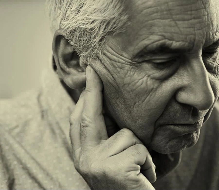 Osoba w podeszłym wieku z problemem ze słuchem myśli o tym, w jaki sposób aparat słuchowy może pomóc w lepszym słyszeniu oraz zrozumieniu mowy w głośnym otoczeniu.